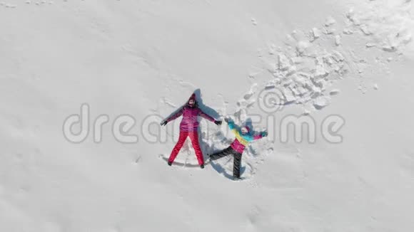年轻的母亲和小女儿在雪地上做天使阳光明媚的冬日欢乐的家庭尽情欢乐视频的预览图