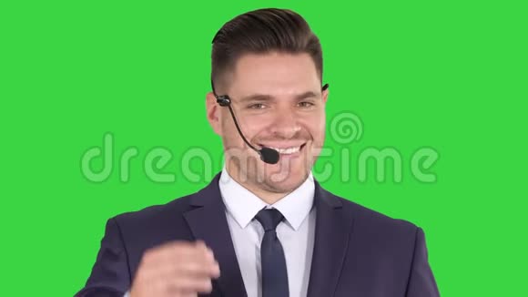英俊的商人带着耳机看着相机在绿色屏幕上微笑Chroma键视频的预览图