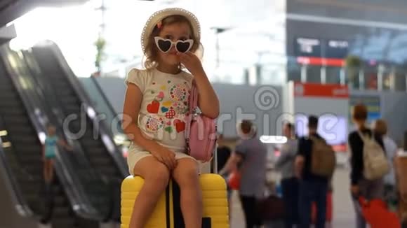 儿童游客坐在火车站的一个黄色的大皮箱上小女孩正在等待出发在视频的预览图