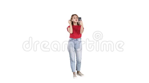 漂亮的年轻女人用睫毛膏在白色背景下看她的智能手机视频的预览图