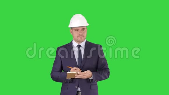 工程师西装和头盔步行和写笔记在记事本上的绿色屏幕铬键视频的预览图