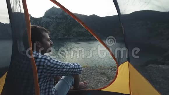 一个年轻人坐在野营帐篷里欣赏美丽的海景和山景克里米亚徒步探险视频的预览图