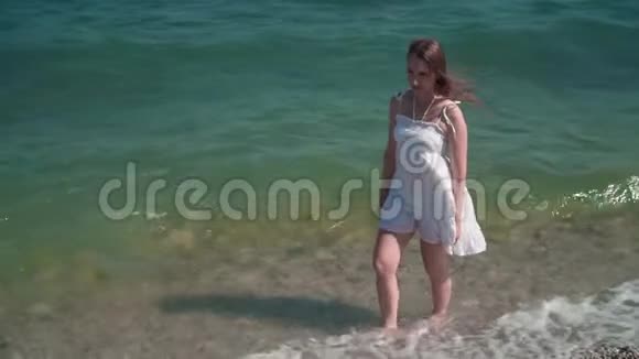一个穿着白色海滩礼服的女孩沿着海滨散步一个光着脚的漂亮女孩沿着海滨散步视频的预览图