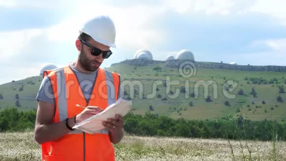 一位身穿白色头盔和背心的男工程师填写文件手里拿着一张纸在此背景下视频的预览图