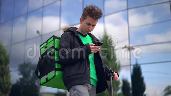 送货员带着绿色的背包和一辆滑板车正在寻找客户电话地址视频的预览图
