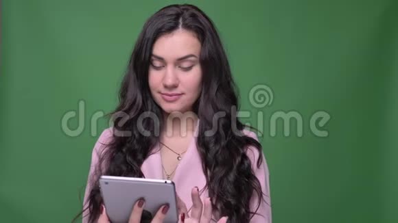 穿着粉红色夹克的布鲁内特女商人展示了蓝色平板电脑屏幕以显示绿色背景上的应用程序视频的预览图