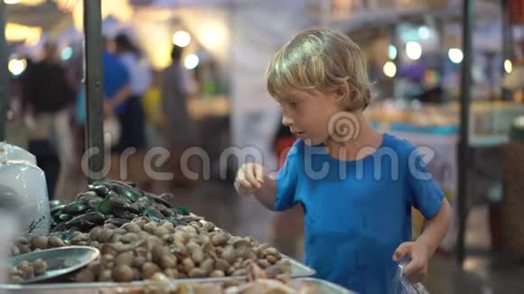 一个小男孩在亚洲街头集市上摸海鞘的慢镜头视频的预览图