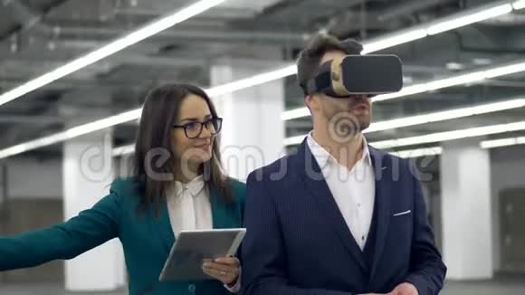 戴着VR眼镜的男性房地产经纪人与一名手持平板电脑的妇女交谈视频的预览图