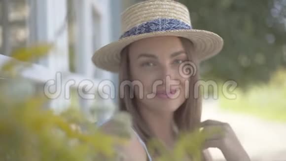 一位戴着草帽的美丽年轻女子的特写镜头看着镜头在户外快乐地微笑着情感乡村视频的预览图
