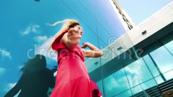 在现代建筑附近跳舞的金发女子的低角度镜头视频的预览图