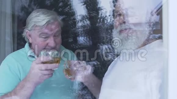 两个喝着酒精威士忌的老人站在家窗户附近白种人老人和朋友在享受时光视频的预览图
