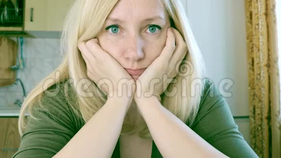 一个悲伤而无聊的年轻金发女人坐在厨房的肖像悲伤和抑郁的概念视频的预览图