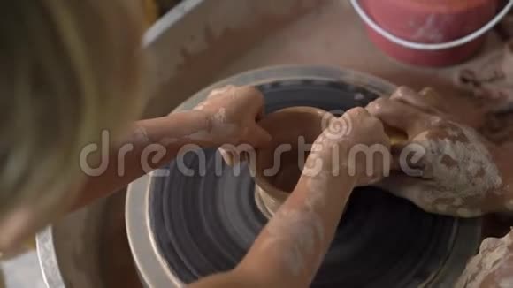 一个教师陶工教他的徒弟如何在陶工的轮子上做一个泥碗的慢速特写镜头视频的预览图