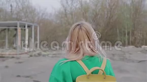 一个穿着绿色毛衣背着背包的女孩是城市里一片废弃的荒地镜头移向她身后视频的预览图