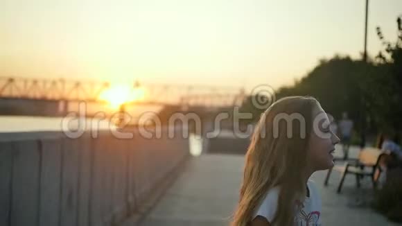 一个留着长发的小女孩在夕阳的照耀下在城市河堤上快乐地跳跃慢动作视频的预览图