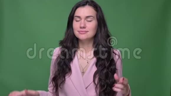 穿着粉红色夹克的布鲁内特女商人用手指示意交叉手指的标志在绿色背景下将希望展现在镜头中视频的预览图