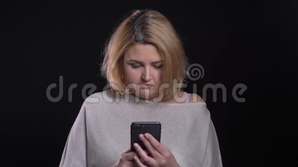 集中的金发短发超重女商人认真观看智能手机的黑色背景视频的预览图