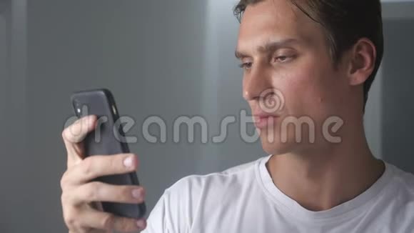 室内魅力男人使用智能手机在社交媒体上发送信息微笑着享受现代生活方式视频的预览图