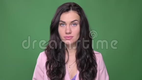 一位身穿粉色夹克的黑发女商人的画像她在绿色背景下平静地看着镜头视频的预览图