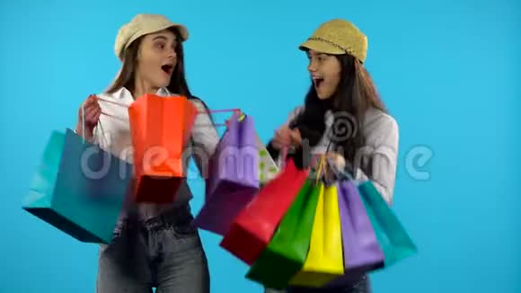 两个幸福的微笑女孩拿着购物袋蓝色背景视频的预览图