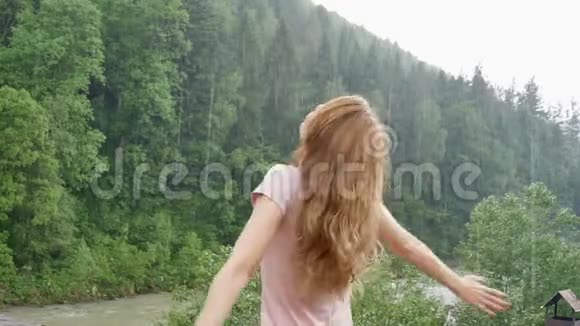 美丽的幸福女孩站在夏雨中在群山覆盖的森林的背景下年轻女子视频的预览图
