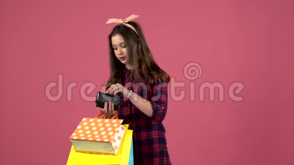 女孩看着购物袋然后钱包已经用完了但有一张卡片粉色背景慢动作视频的预览图