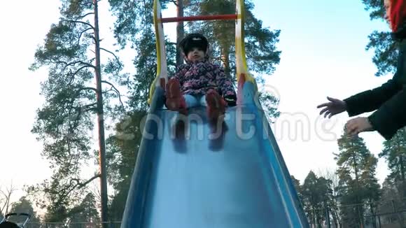 一个穿着五颜六色夹克的小女孩在春天公园里妈妈的帮助下从一多颜色的滑梯上下来视频的预览图