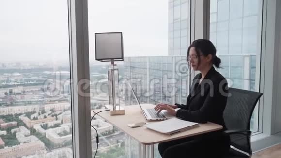 商务女性坐在办公室的窗户旁用电脑工作一位身着商务服装的年轻女子的肖像视频的预览图