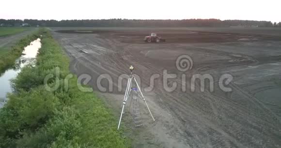 经纬仪和拖拉机犁肥沃的田野土壤上景视频的预览图