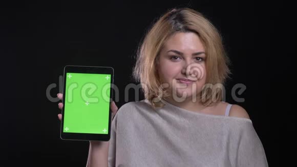 金发短发超重的女商人展示绿色平板电脑屏幕在黑色背景上展示应用程序视频的预览图