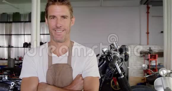 男子机械师双臂交叉站立在摩托车修理车库4k视频的预览图