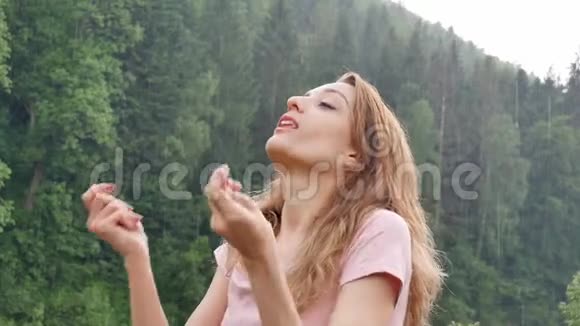 美丽的幸福女孩站在夏雨中在群山覆盖的森林的背景下年轻女子视频的预览图