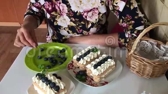 一个女人装饰用萨沃亚迪饼干和奶油做的蛋糕用蓝莓和薄荷装饰视频的预览图