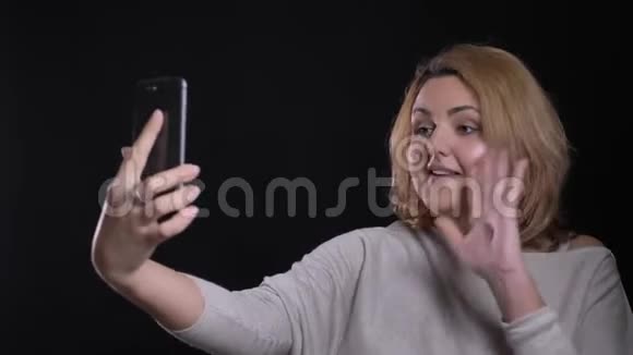 可爱的金发短发超重的女商人在黑色背景的智能手机上愉快地在视频聊天视频的预览图