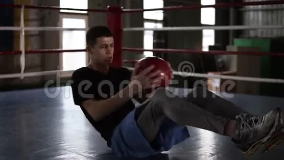 运动的年轻人在拳击场的地板上做腹部运动一个人用药球锻炼身体视频的预览图