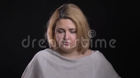 金发短发超重的商务女性吹着脸颊悲伤地在黑色背景下往下看视频的预览图