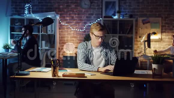 快乐的人在黑暗的办公室里使用笔记本电脑享受着商业的成功微笑着视频的预览图