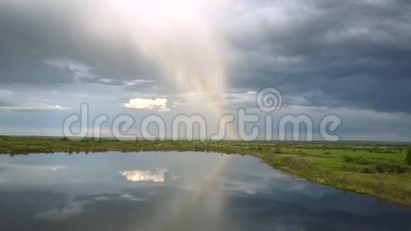 在平静的湖泊和草地上巨大的彩虹和浓密的云视频的预览图