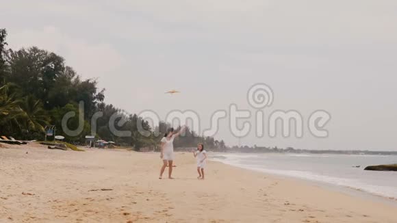 快乐的小女孩放风筝和年轻的妈妈一起奔向相机在异国情调的海滩热带度假慢动作视频的预览图