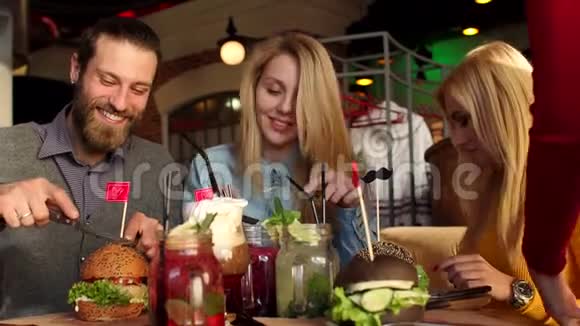 漂亮的女孩和开朗的男孩坐在一起吃汉堡视频的预览图