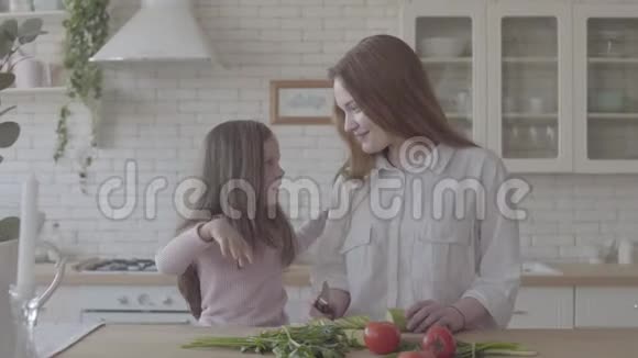 肖像美丽的年轻母亲和她可爱的小女儿在大厨房女人做饭和小女孩吻她视频的预览图
