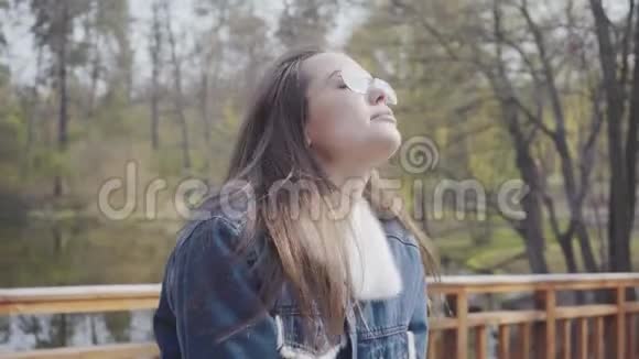 穿着牛仔裤夹克的年轻可爱女子站在木桥上环视镜头然后起飞的肖像视频的预览图