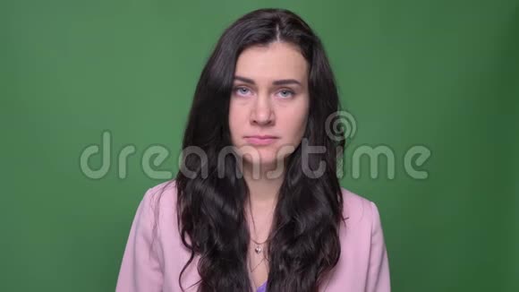 身着粉红色夹克的黑发女商人的肖像在绿色背景下带着巨大的痛苦和悲伤进入镜头视频的预览图