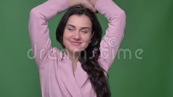 年轻的黑发女性vloger穿着粉红色夹克在绿色背景下满意地跳舞进入相机的肖像视频的预览图