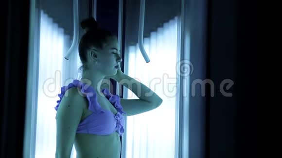 日光浴室穿着紫色泳衣在垂直日光浴室晒黑的美丽少女视频的预览图