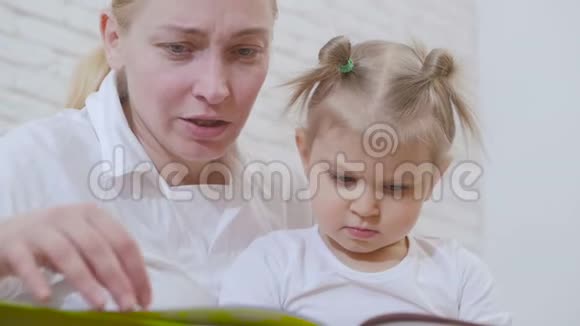 一个女人在为一个坐沙发上的小女孩读一本儿童读物视频的预览图