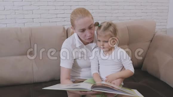 一个女人在为一个坐沙发上的小女孩读一本儿童读物视频的预览图