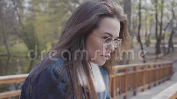 年轻迷人的女士穿着牛仔裤夹克站在木桥上四处张望镜头拍摄视频的预览图