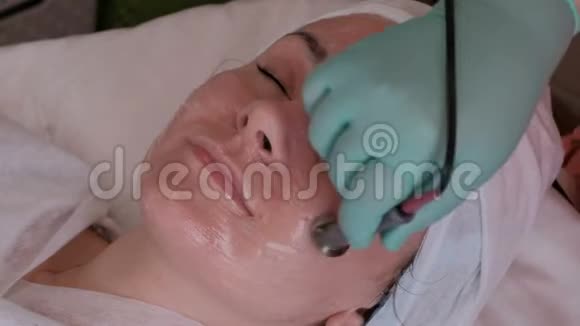 美容院电流的使用美容师的双手在年轻妇女的脸上涂电极视频的预览图