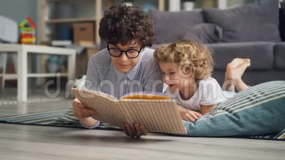 幸福的家庭年轻的女人和小男孩躺在家里的毯子上看书视频的预览图
